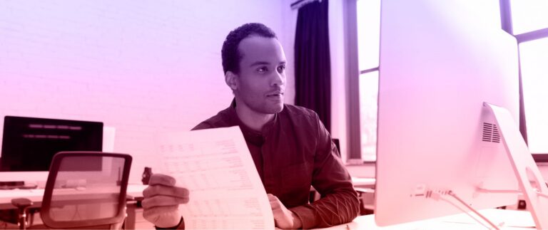A man sits at a desk, focused on a piece of paper in front of him.