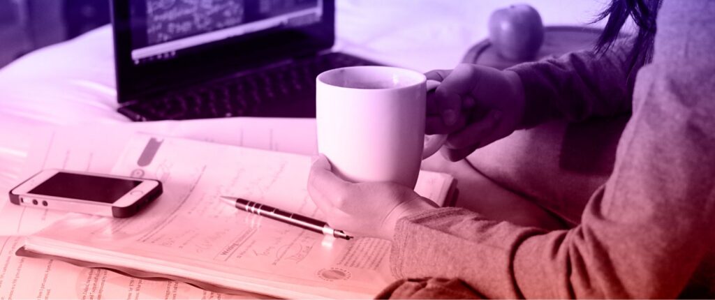 A person sitting on a bed, using a laptop while holding a cup, creating a cozy work or relaxation environment.